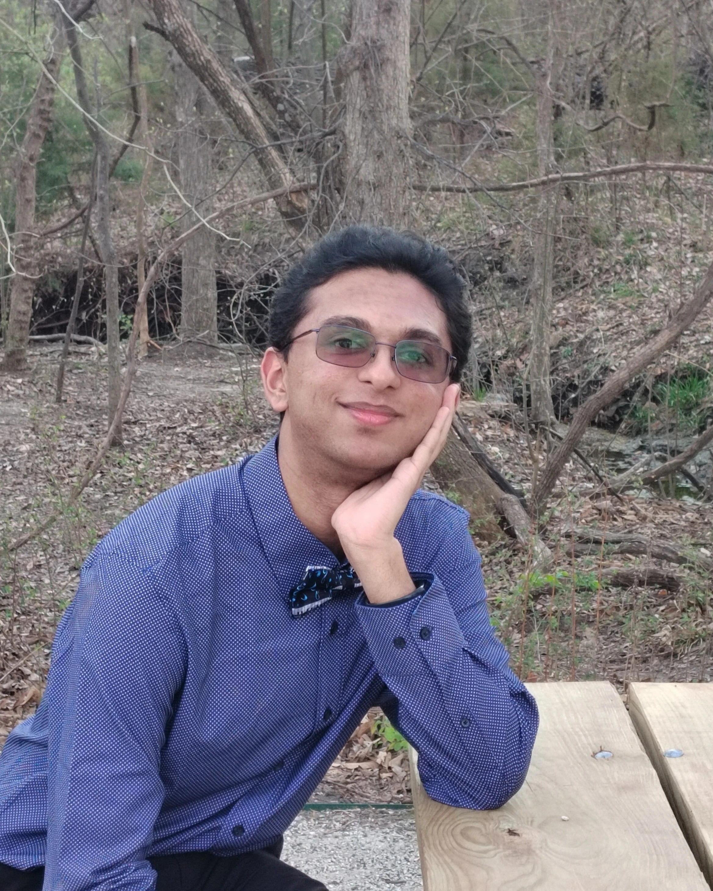 Rishi Venkatesh sitting on a picnic table bench in front of a forest